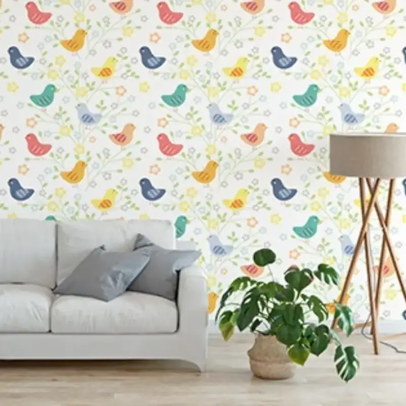 A cozy living room with a white sofa, gray cushions, a green potted plant, and a floor lamp. The wall features colorful bird and floral patterned wallpaper on a white background, expertly crafted through quality printing services.